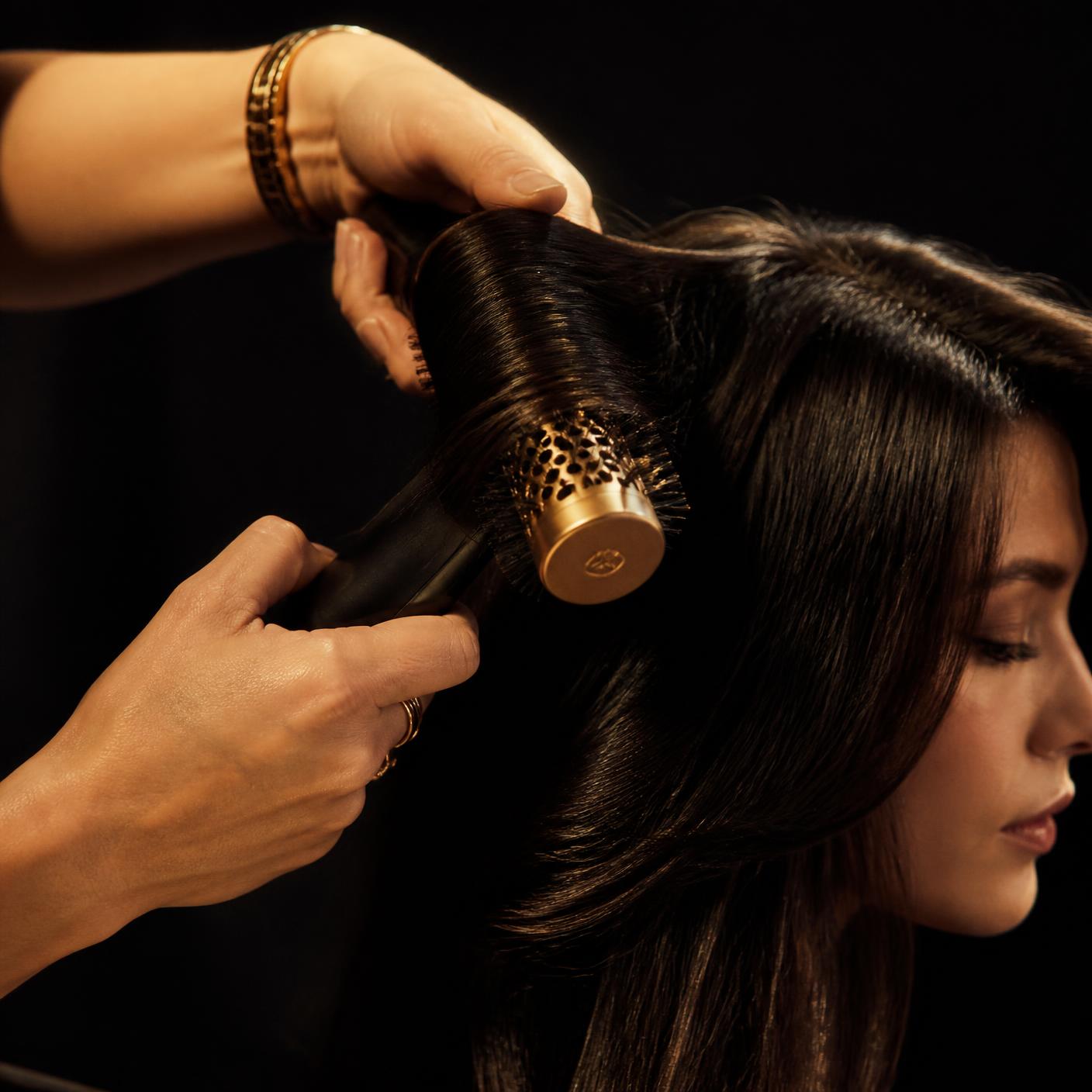 Stylist styling long dark hair with a gold round brush