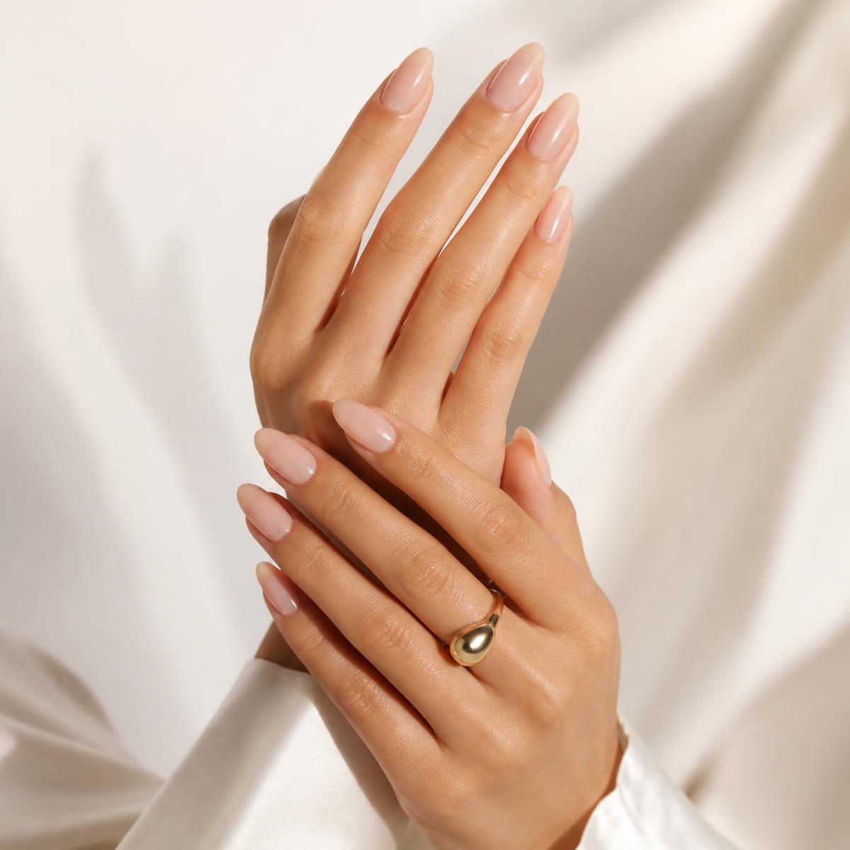 Elegant manicured hands with glossy nude almond nails and a gold ring
